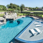 An image of a stunning backyard pool featuring a wading area, a grotto, a waterfall, and a spa