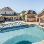 An image of a stunning backyard pool featuring a wading area, a grotto, a waterfall, and a spa